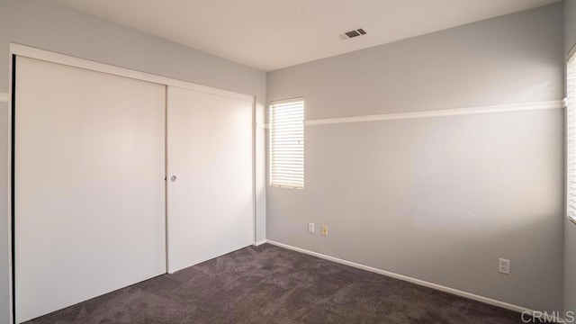 unfurnished bedroom featuring dark carpet and a closet