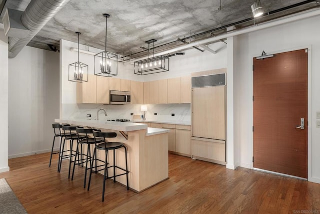 kitchen with a breakfast bar, hanging light fixtures, light brown cabinets, paneled refrigerator, and hardwood / wood-style flooring