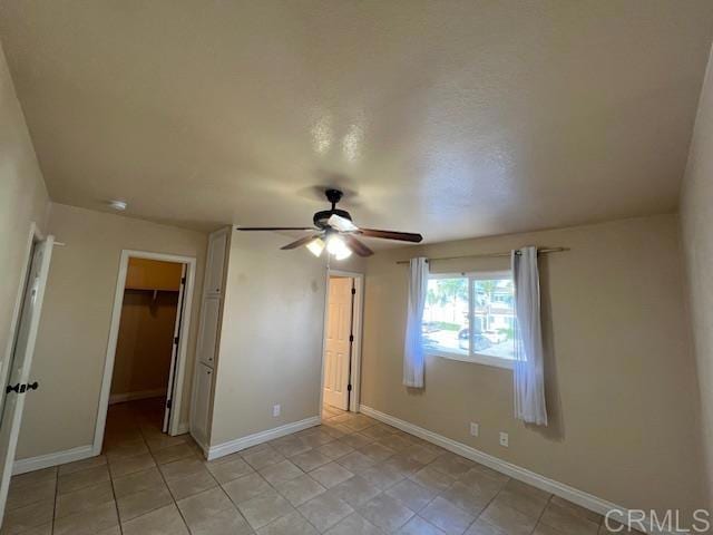 unfurnished bedroom featuring light tile patterned floors, a closet, a spacious closet, a ceiling fan, and baseboards