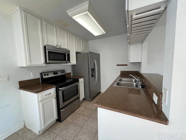 kitchen with light tile patterned floors, dark countertops, stainless steel appliances, white cabinetry, and a sink