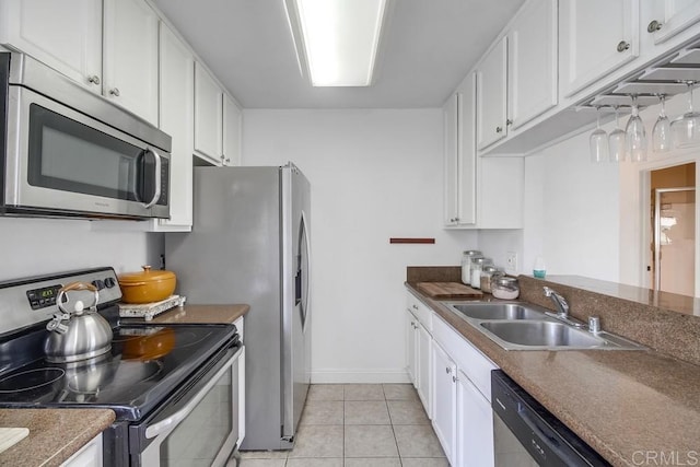 kitchen featuring light tile patterned floors, baseboards, white cabinets, appliances with stainless steel finishes, and a sink