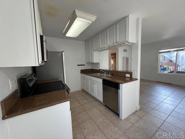 kitchen with stainless steel appliances, dark countertops, light tile patterned flooring, and a sink