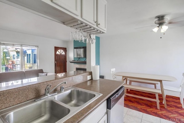 kitchen with a sink, white cabinets, stainless steel dishwasher, dark countertops, and a glass covered fireplace