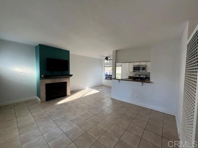 unfurnished living room with light tile patterned floors, baseboards, a ceiling fan, and a tiled fireplace