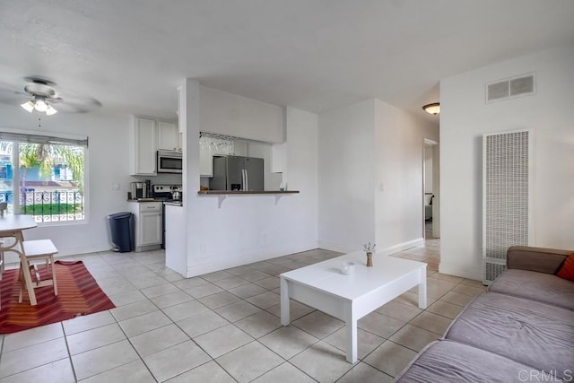 living room with light tile patterned floors, visible vents, baseboards, a ceiling fan, and a heating unit