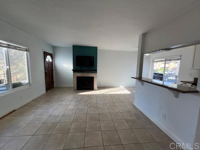 unfurnished living room with a fireplace, baseboards, and light tile patterned floors