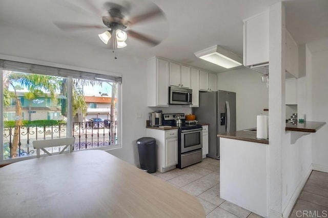 kitchen with light tile patterned floors, white cabinets, dark countertops, ceiling fan, and stainless steel appliances