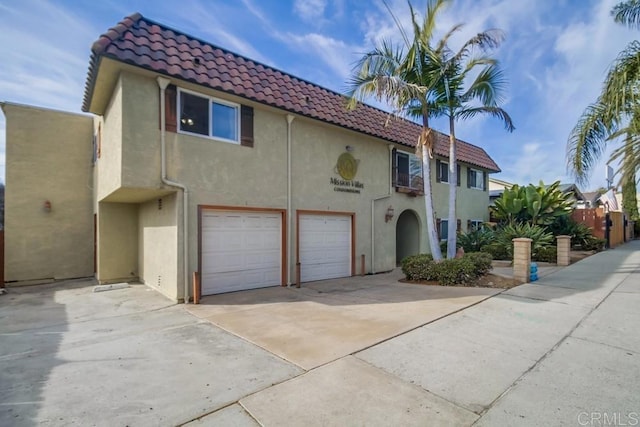 mediterranean / spanish house featuring a garage, driveway, a tile roof, and stucco siding