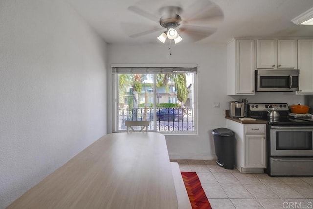 kitchen with light tile patterned floors, ceiling fan, white cabinets, appliances with stainless steel finishes, and dark countertops