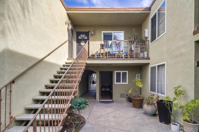 view of exterior entry featuring a patio, a balcony, and stucco siding