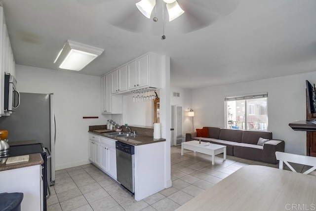 kitchen with light tile patterned floors, stainless steel appliances, a sink, open floor plan, and dark countertops