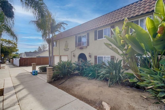 view of front facade featuring concrete driveway, a tiled roof, an attached garage, fence, and stucco siding