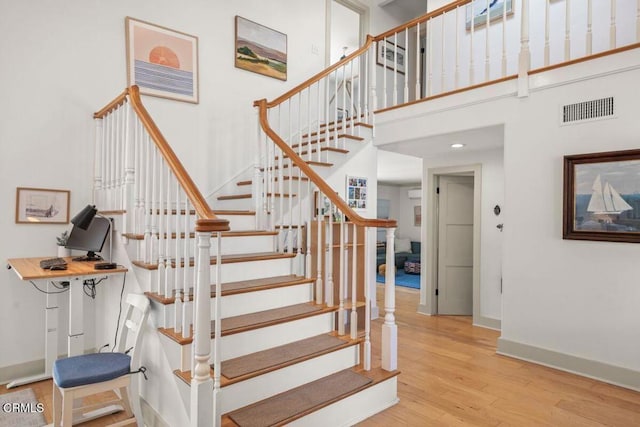 stairway with hardwood / wood-style flooring and a towering ceiling