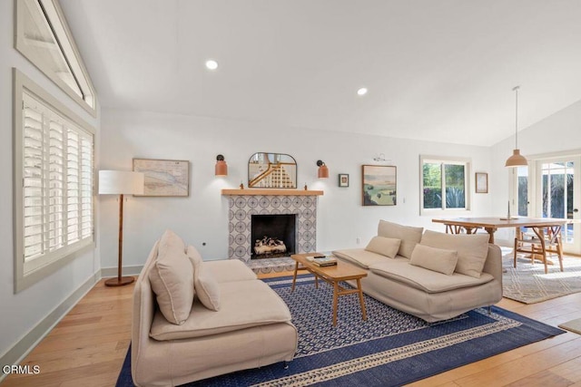 living room featuring a tile fireplace, lofted ceiling, and light hardwood / wood-style floors