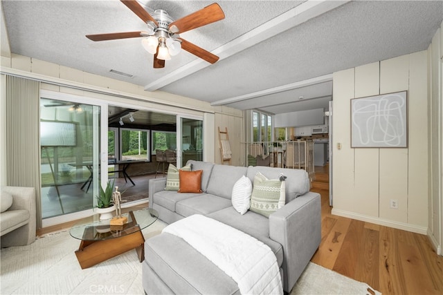 living room with beamed ceiling, ceiling fan, a textured ceiling, and light hardwood / wood-style flooring