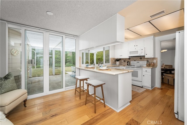 kitchen featuring tasteful backsplash, white cabinetry, a breakfast bar area, light hardwood / wood-style floors, and white appliances