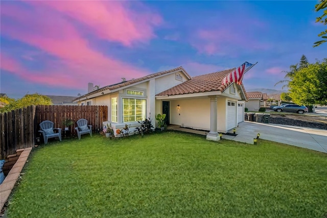 back house at dusk with a garage and a lawn