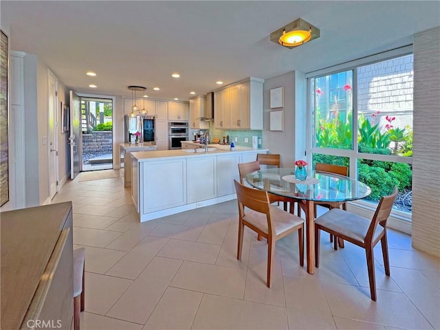 kitchen featuring pendant lighting, stainless steel double oven, backsplash, a center island, and wall chimney exhaust hood