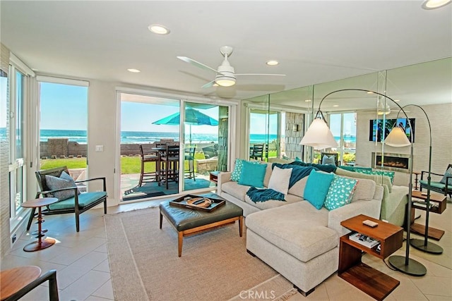 tiled living room featuring floor to ceiling windows, a large fireplace, ceiling fan, and a water view