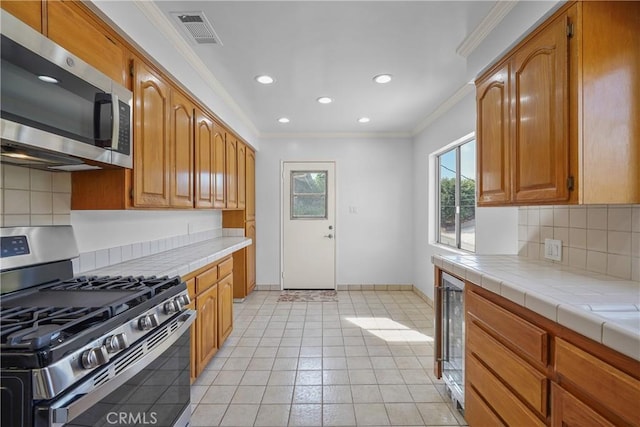 kitchen featuring visible vents, tile countertops, ornamental molding, brown cabinets, and stainless steel appliances