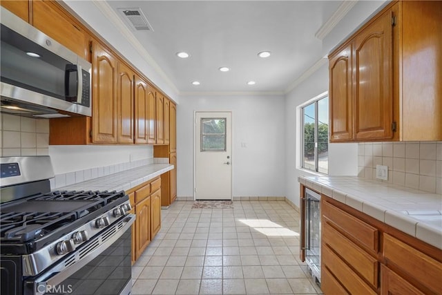 kitchen featuring visible vents, stainless steel appliances, tile counters, crown molding, and tasteful backsplash