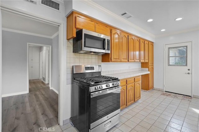 kitchen featuring tasteful backsplash, visible vents, crown molding, tile countertops, and stainless steel appliances