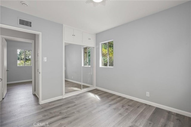 unfurnished bedroom with baseboards, multiple windows, visible vents, and light wood finished floors