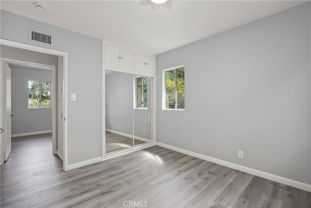 unfurnished bedroom featuring visible vents, multiple windows, baseboards, and wood finished floors