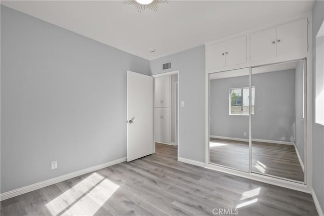 unfurnished bedroom featuring a closet, visible vents, baseboards, and wood finished floors