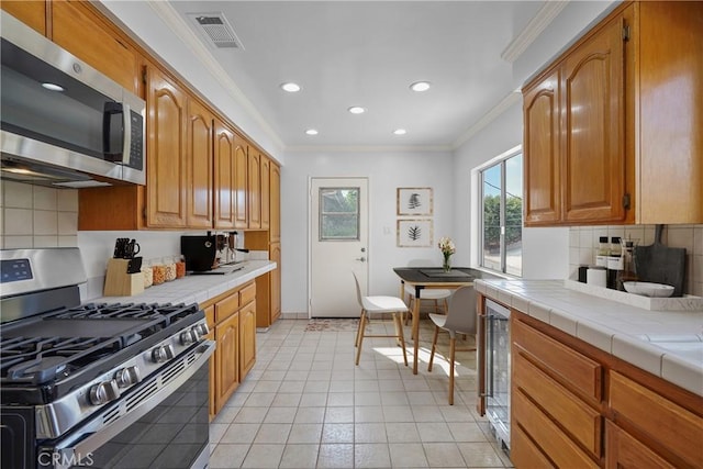 kitchen with visible vents, tile countertops, appliances with stainless steel finishes, crown molding, and backsplash