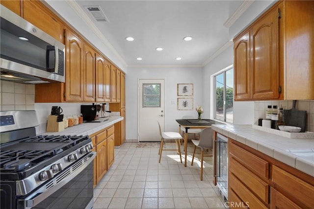 kitchen featuring visible vents, backsplash, appliances with stainless steel finishes, crown molding, and tile counters