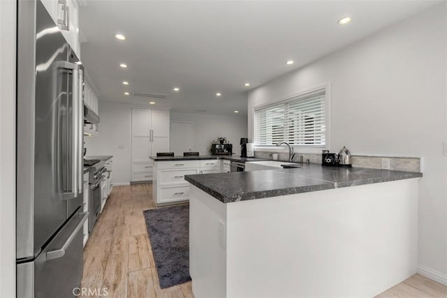 kitchen featuring high end appliances, dark countertops, white cabinetry, a sink, and a peninsula