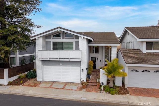 view of front of house with a garage, driveway, brick siding, and a balcony