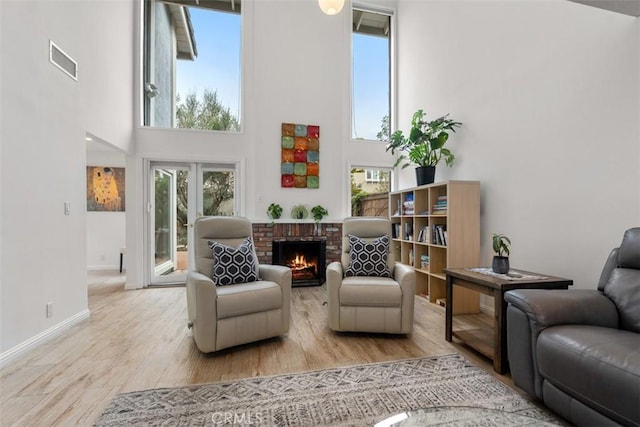 sitting room with baseboards, visible vents, a towering ceiling, light wood-type flooring, and a brick fireplace