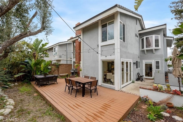 rear view of property with a deck, outdoor dining area, fence, and stucco siding