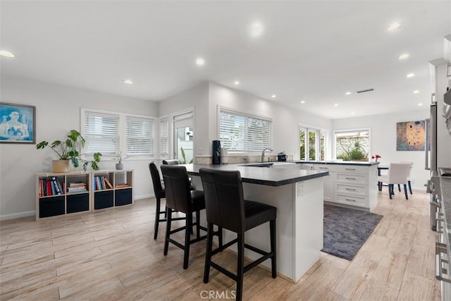 kitchen featuring a breakfast bar area, dark countertops, light wood-style floors, white cabinetry, and a kitchen island