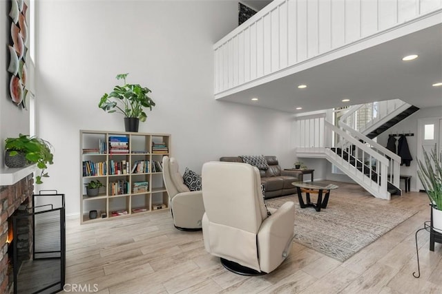 living area with a brick fireplace, light wood finished floors, a high ceiling, and stairs