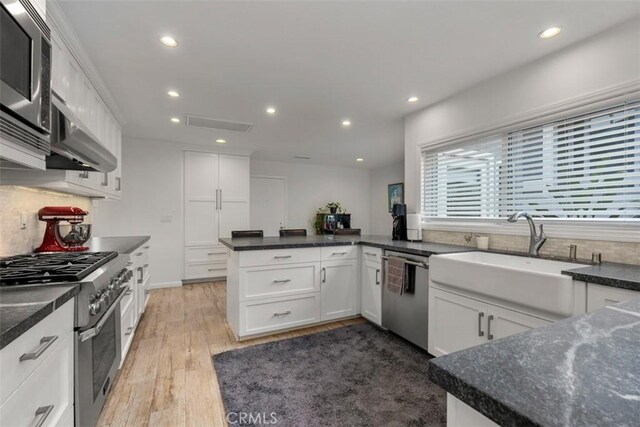 kitchen with sink, appliances with stainless steel finishes, white cabinetry, wood-type flooring, and exhaust hood