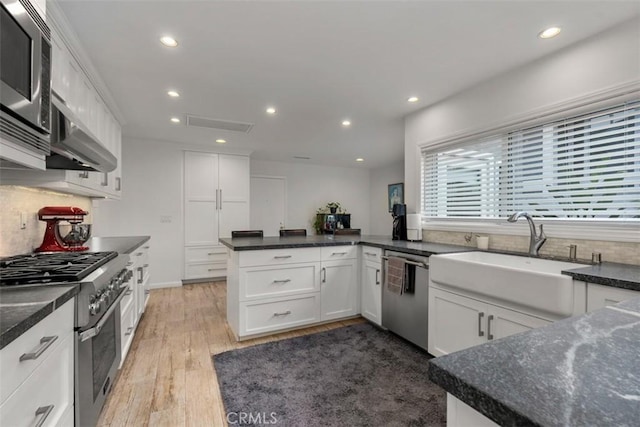 kitchen featuring stainless steel appliances, white cabinets, a sink, wood finished floors, and exhaust hood