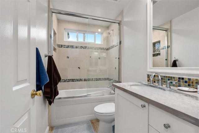 bathroom with decorative backsplash, combined bath / shower with glass door, vanity, and toilet