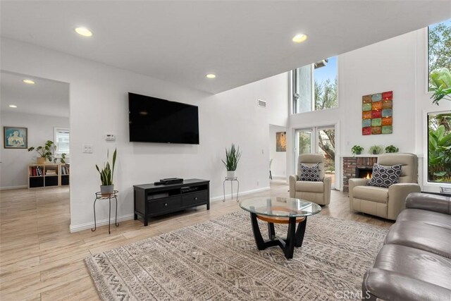 living room with a towering ceiling, a healthy amount of sunlight, a fireplace, and light hardwood / wood-style floors