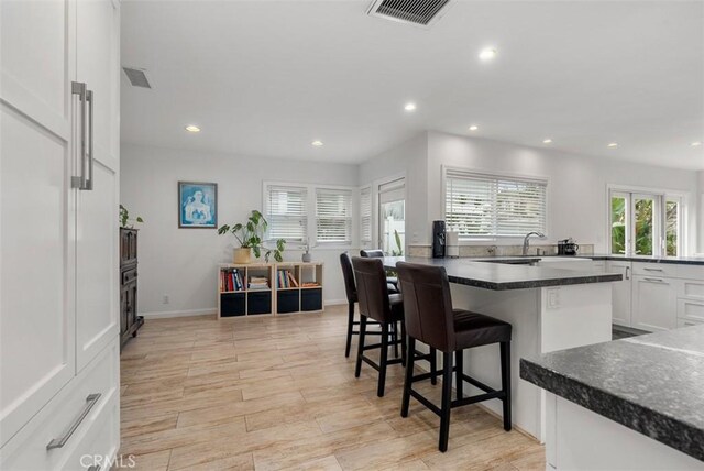 kitchen with white cabinetry, a kitchen island, sink, and a kitchen bar