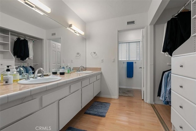 bathroom featuring double vanity, visible vents, wood finished floors, a spacious closet, and a sink