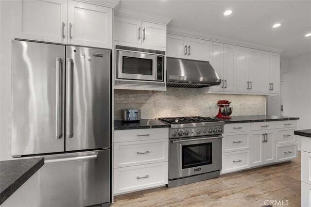 kitchen with tasteful backsplash, stainless steel appliances, dark stone counters, and white cabinets