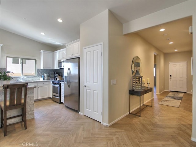 kitchen featuring white cabinetry, tasteful backsplash, vaulted ceiling, appliances with stainless steel finishes, and light parquet flooring