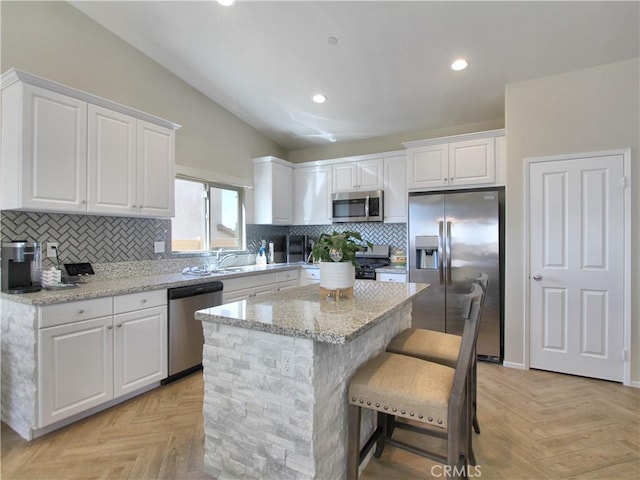 kitchen featuring appliances with stainless steel finishes, white cabinetry, a center island, light stone counters, and light parquet flooring