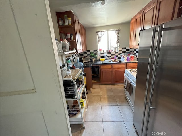 kitchen with tasteful backsplash, white gas range, sink, high end refrigerator, and light tile patterned floors