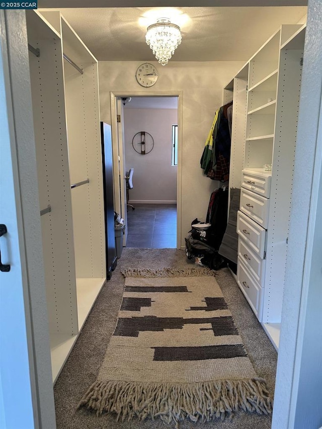 walk in closet featuring a notable chandelier and dark carpet