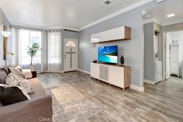 living room with stacked washer and dryer, ornamental molding, and light hardwood / wood-style floors