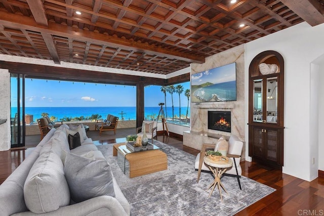 living room with dark wood-type flooring, coffered ceiling, a water view, beamed ceiling, and a high end fireplace